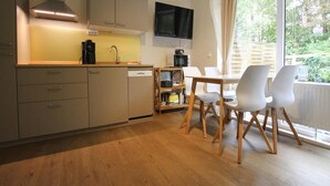 A compact kitchen with a dining area, wooden cabinets, a built-in microwave, and a large window with curtains. - Apartment, St. Peter-ording (St. Peter-Ording)
