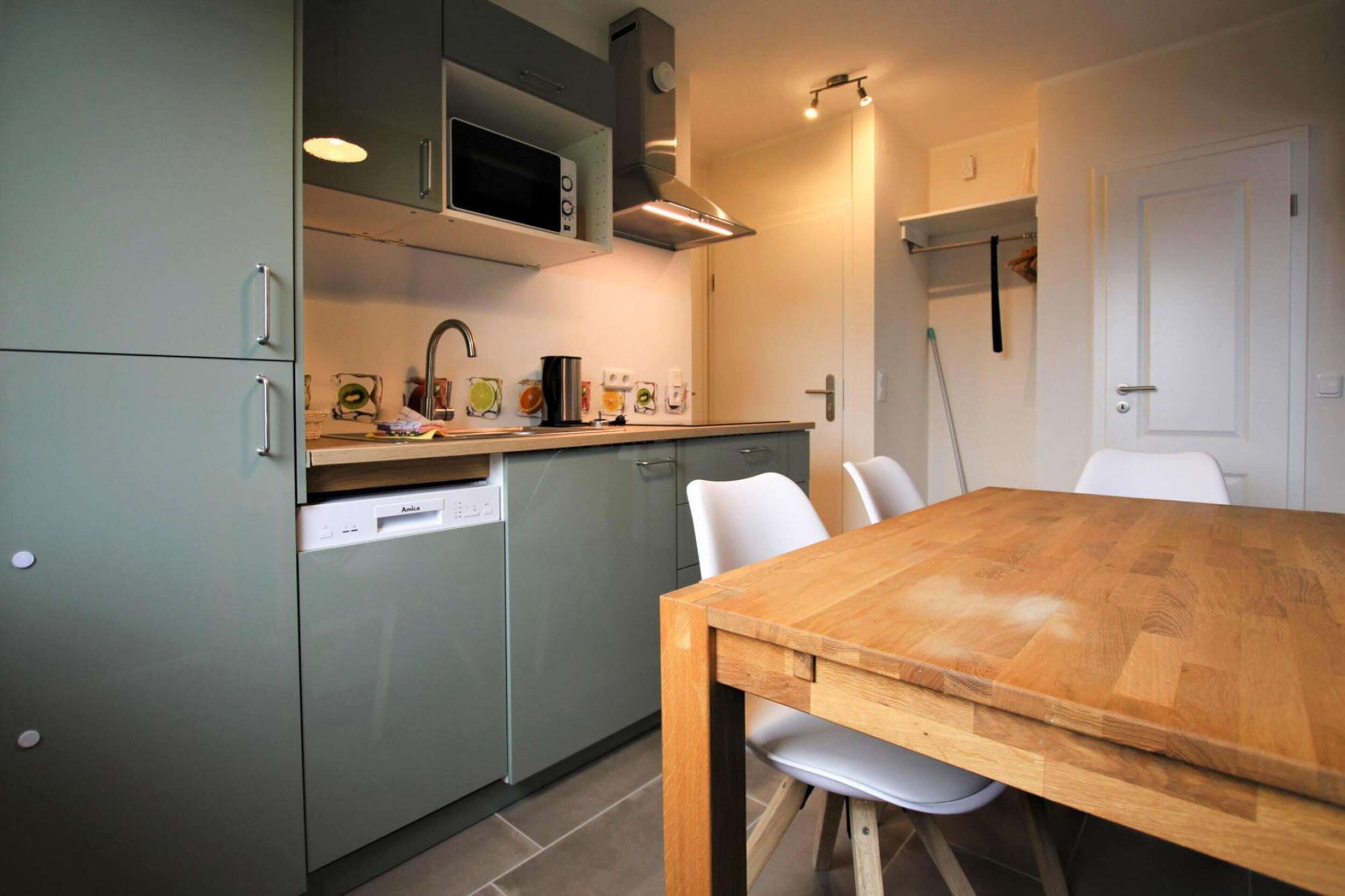 A modern kitchen with a wooden table and white chairs, a dishwasher, and a microwave above the sink.