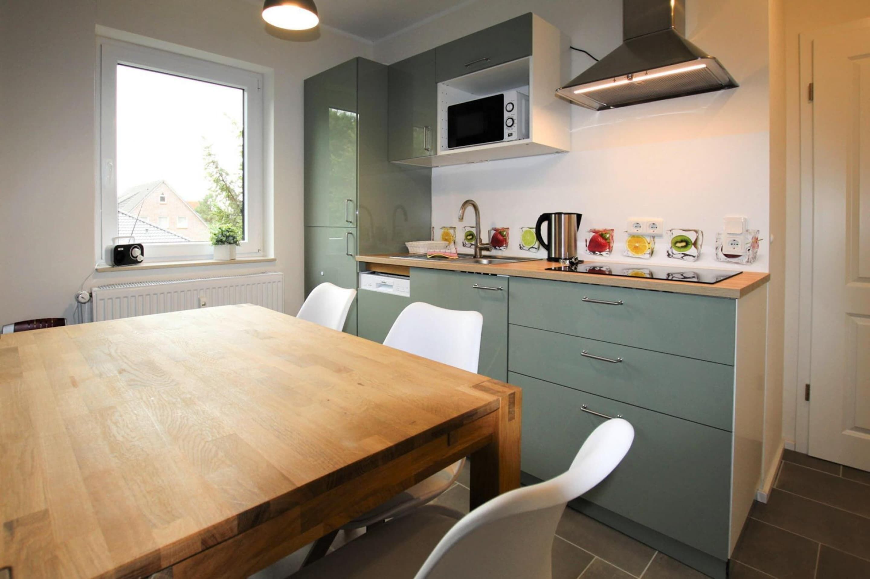 Une cuisine moderne avec une table à manger en bois, des chaises blanches, un four à micro-ondes encastré et une fenêtre donnant sur des immeubles.