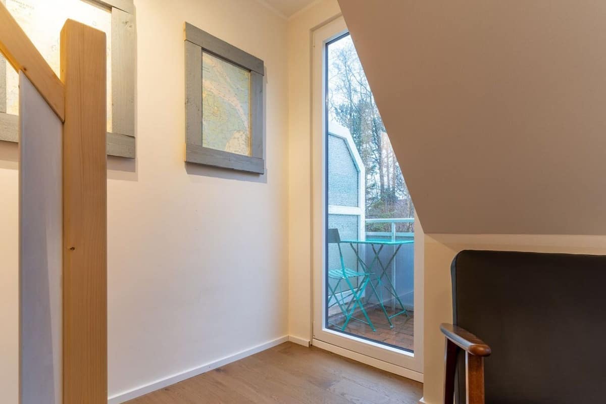 A room with a wooden floor, a framed map on the wall, and a window overlooking a balcony with outdoor furniture.