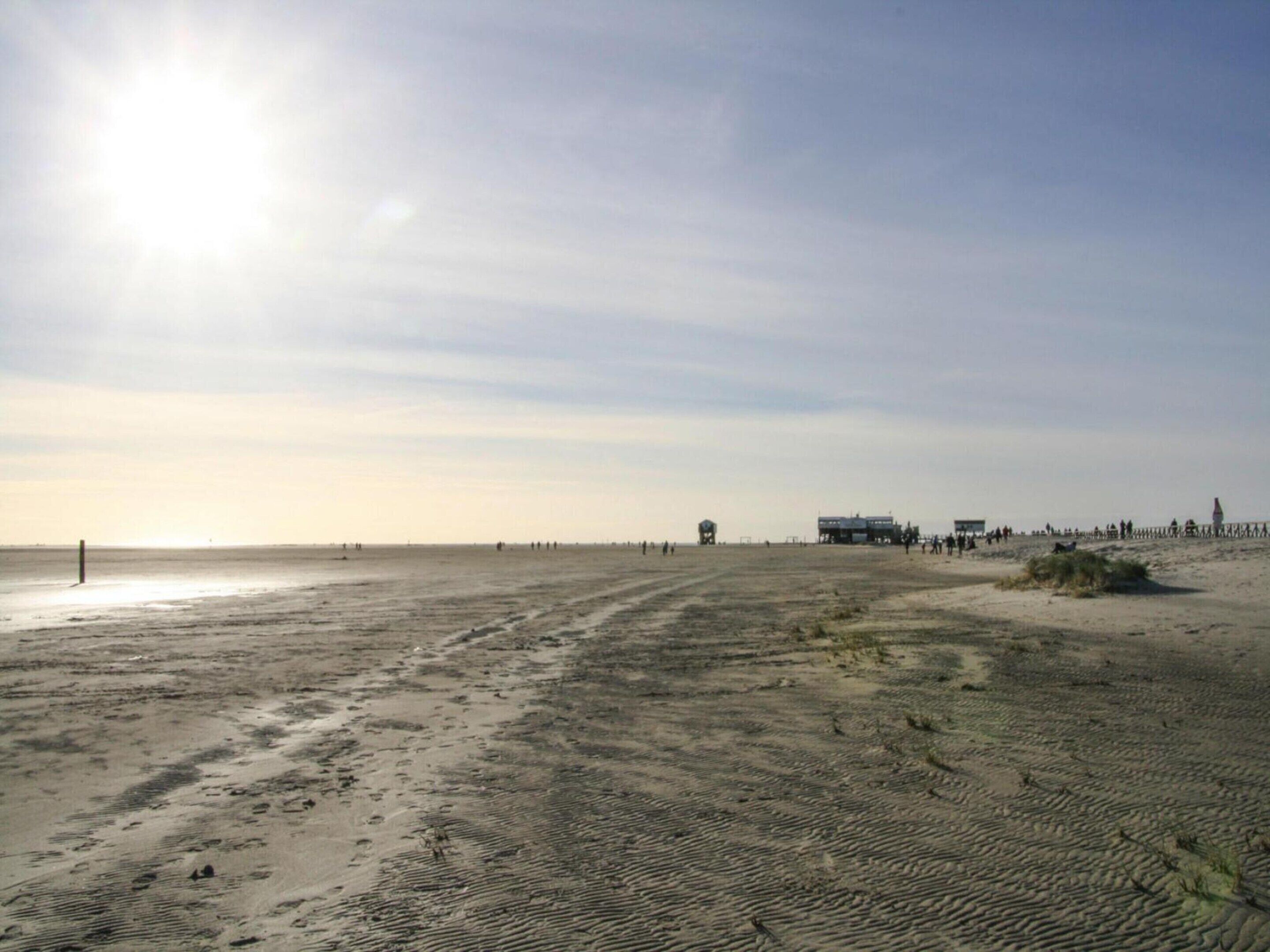 A wide sandy beach with a few structures in the distance, including a lifeguard tower and a building that could be a lifeguard station.