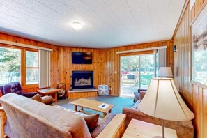 A cozy cabin interior with a fireplace, wooden walls, and large windows. - Pine & Paddle PLUS (Saint Germain)