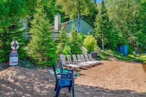 A beach area with lounge chairs, a pile of sand, and a house in the background. - Pine & Paddle PLUS (Saint Germain)