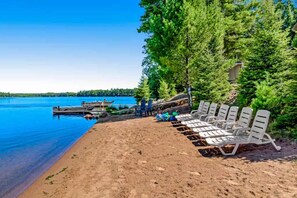 A beach with white lounge chairs, a dock, and a clear blue lake. - Pine & Paddle PLUS (Saint Germain)