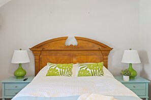 A neatly made bed with a wooden headboard, two bedside tables with lamps, and green decorative pillows.