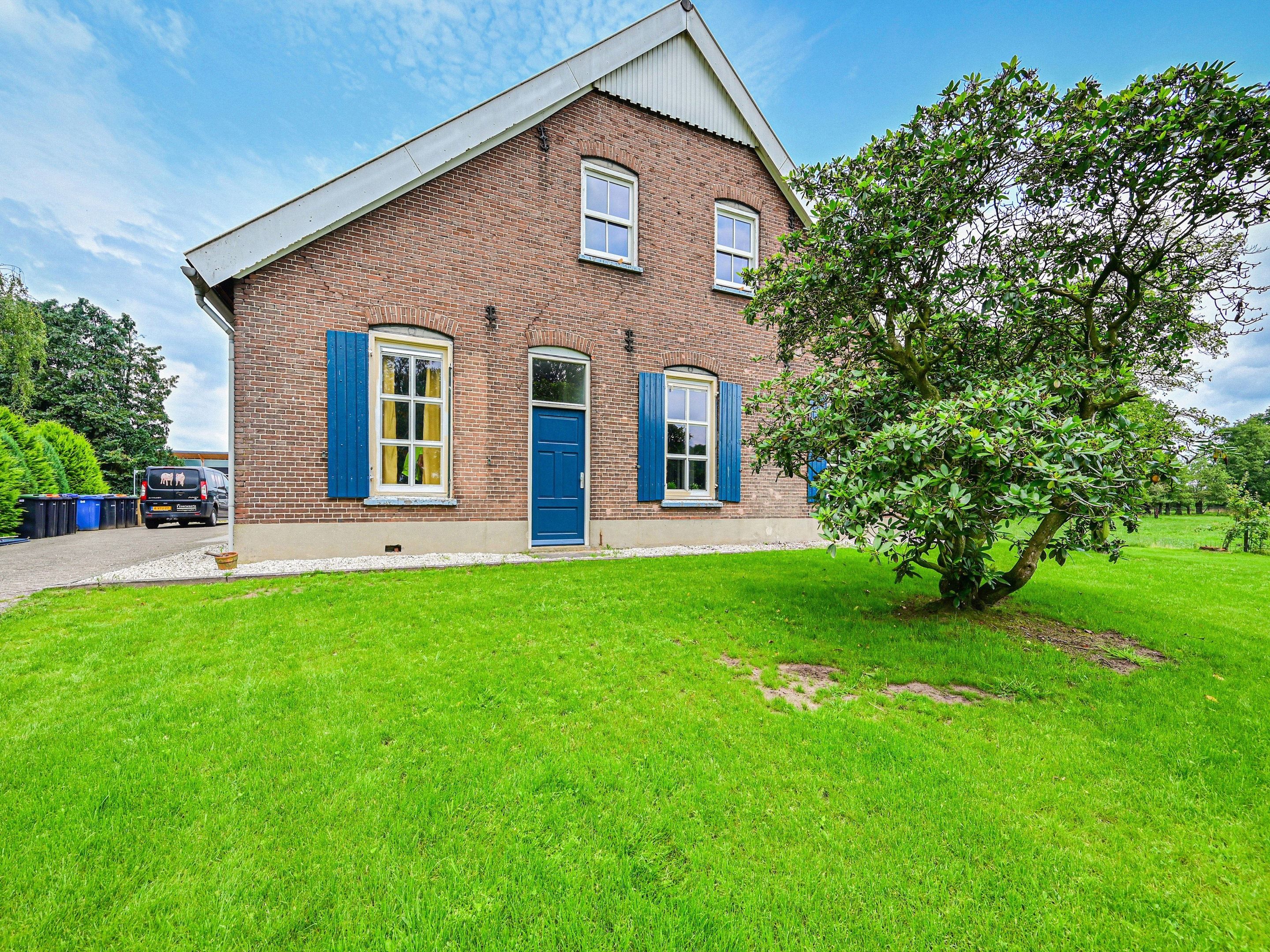 A two-story brick house with a blue door and shutters, a small front yard, and a tree.