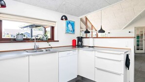 Ett modernt kök med vita skåp, en diskho i rostfritt stål och ett fönster med utsikt över ett bostadsområde.