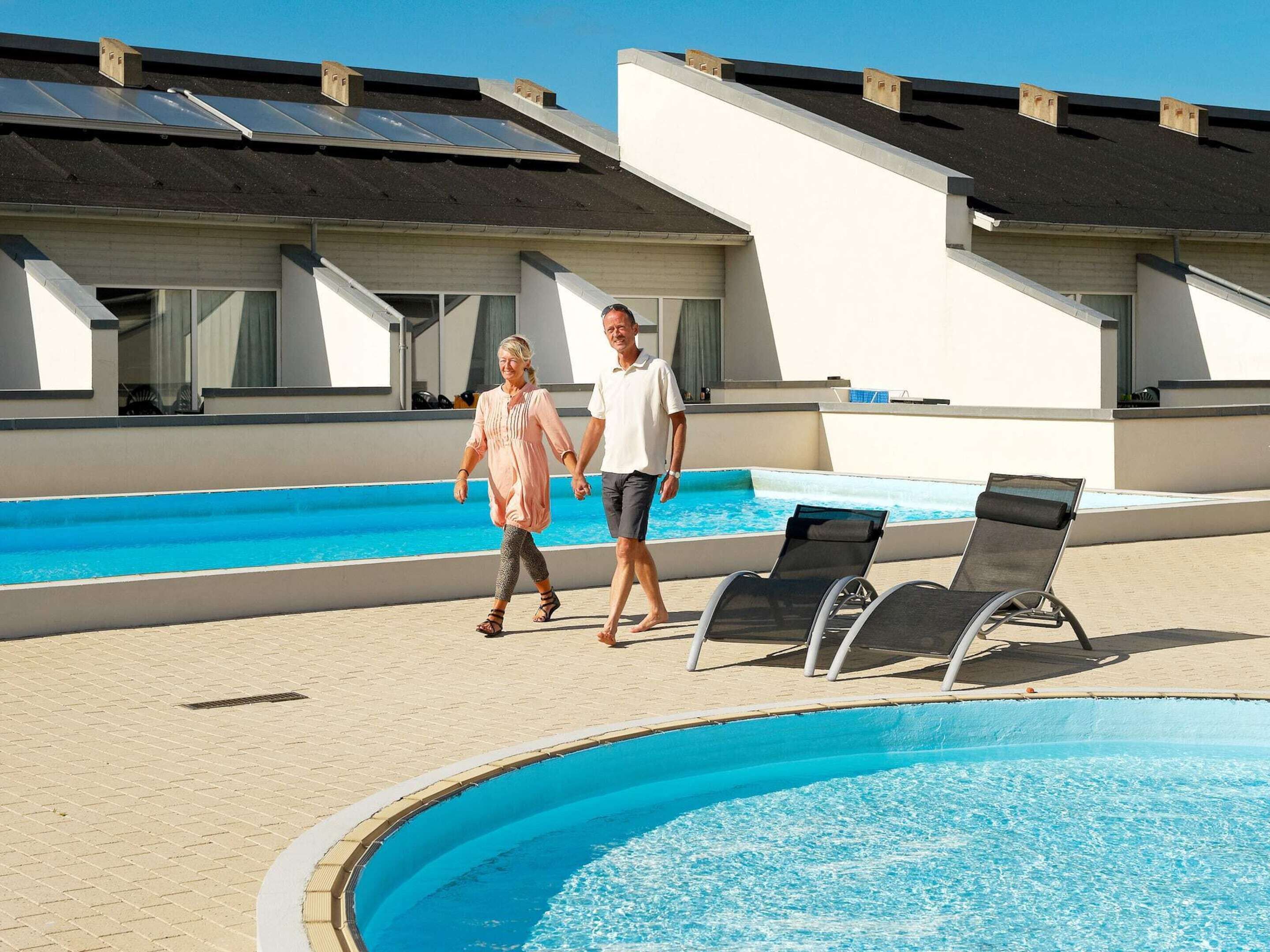 A swimming pool area with lounge chairs, a pool, and a building with solar panels.