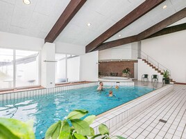 Una piscina interior con agua azul cristalina, suelo de baldosas y una pared de ladrillo al fondo.