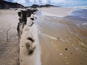 Une plage avec une étroite bande de sable qui mène à l’eau, entourée d’un paysage rocheux.