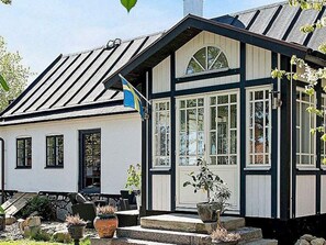 Ett traditionellt hus med ett sadeltak, en veranda med trappsteg och en krukväxt.