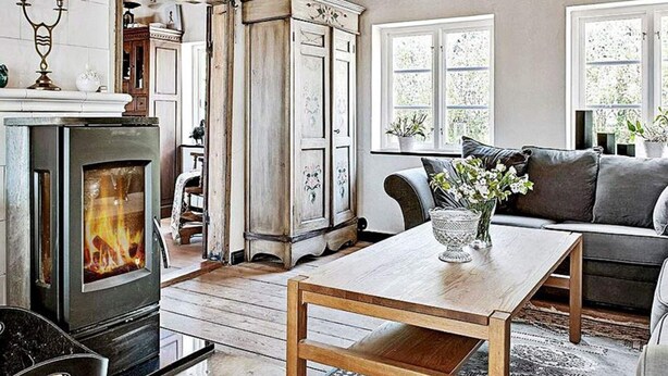 A cozy living room with a fireplace, wooden furniture, and a view of the outdoors through large windows. - 4 Person Holiday Home in Kivik (Kivik)