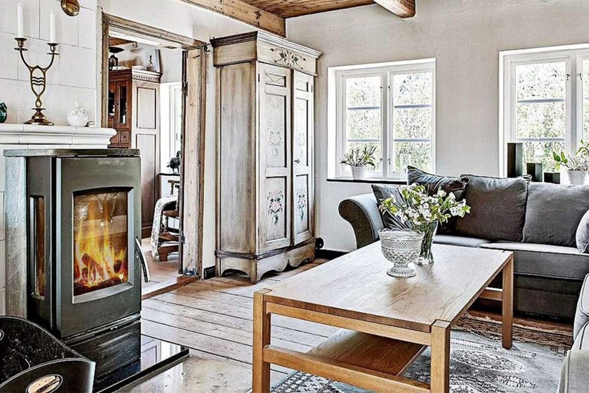 A cozy living room with a fireplace, wooden furniture, and a view of the outdoors through large windows.
