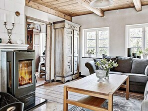 A cozy living room with a fireplace, wooden furniture, and a view of the outdoors through large windows. - 4 Person Holiday Home in Kivik (Kivik)