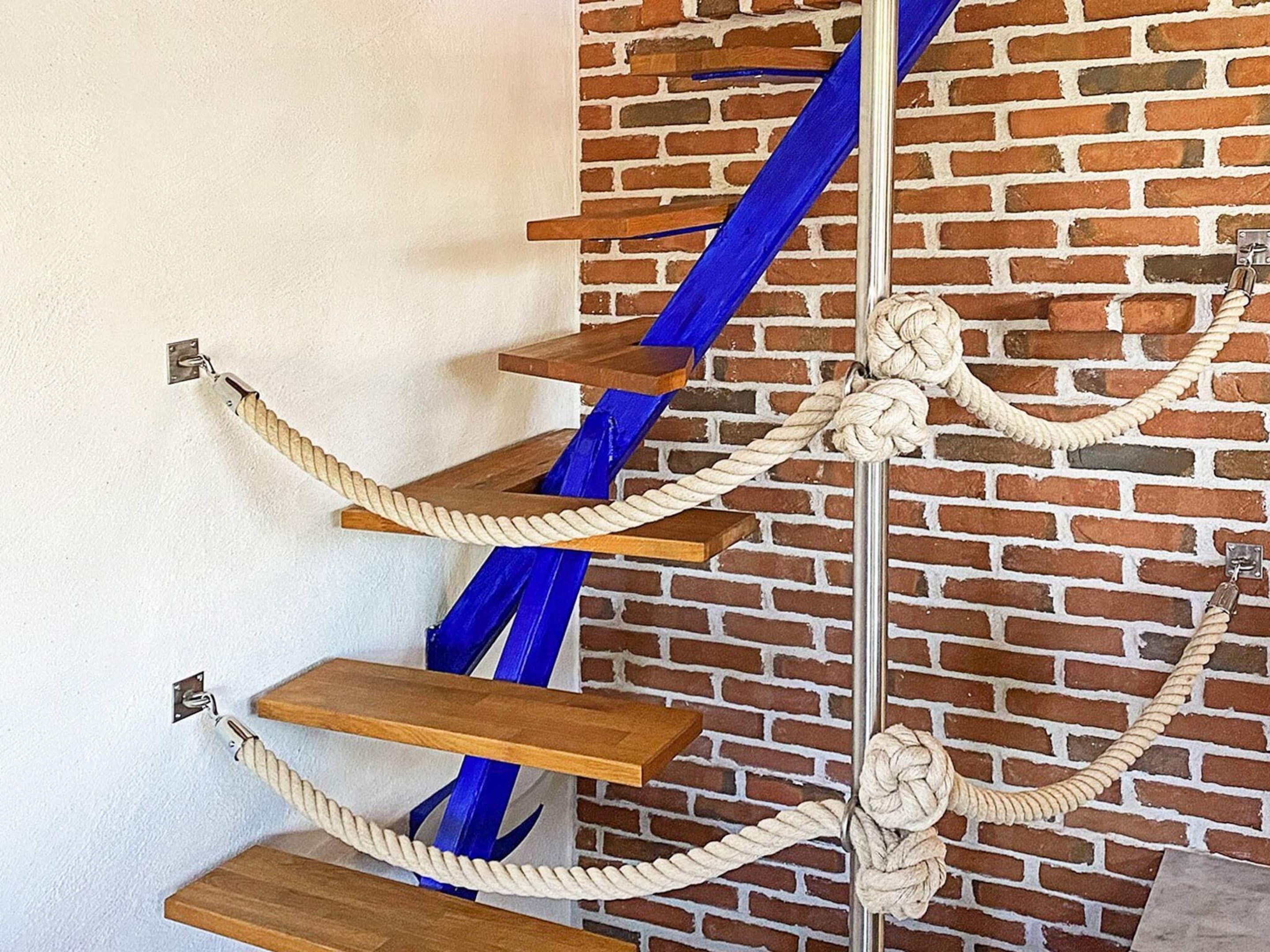 A wooden staircase with blue accents and rope handrails against a brick wall.