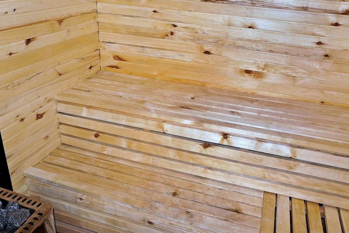 A wooden interior with horizontal slats, a small bench, and a stone fireplace.
