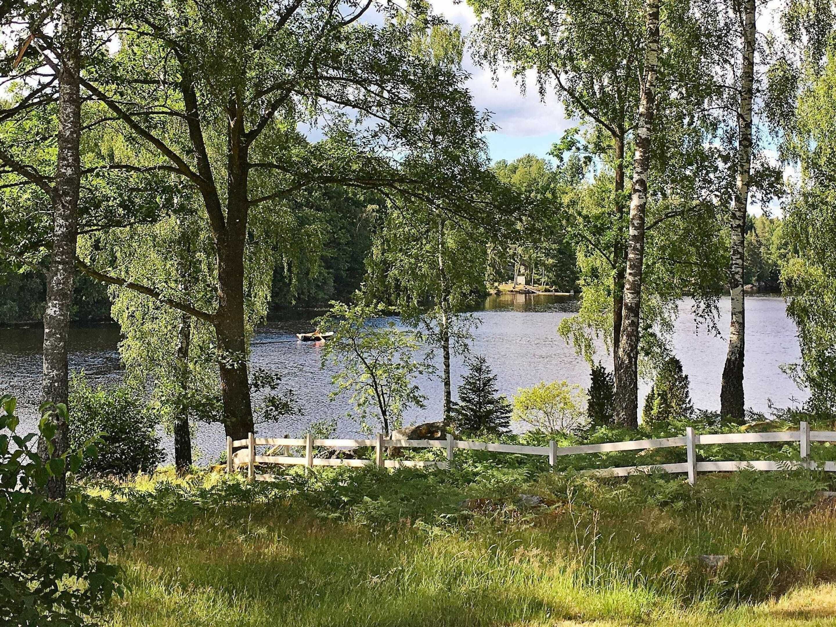 A serene lakeside view with a wooden dock extending into the water, surrounded by lush greenery and trees.