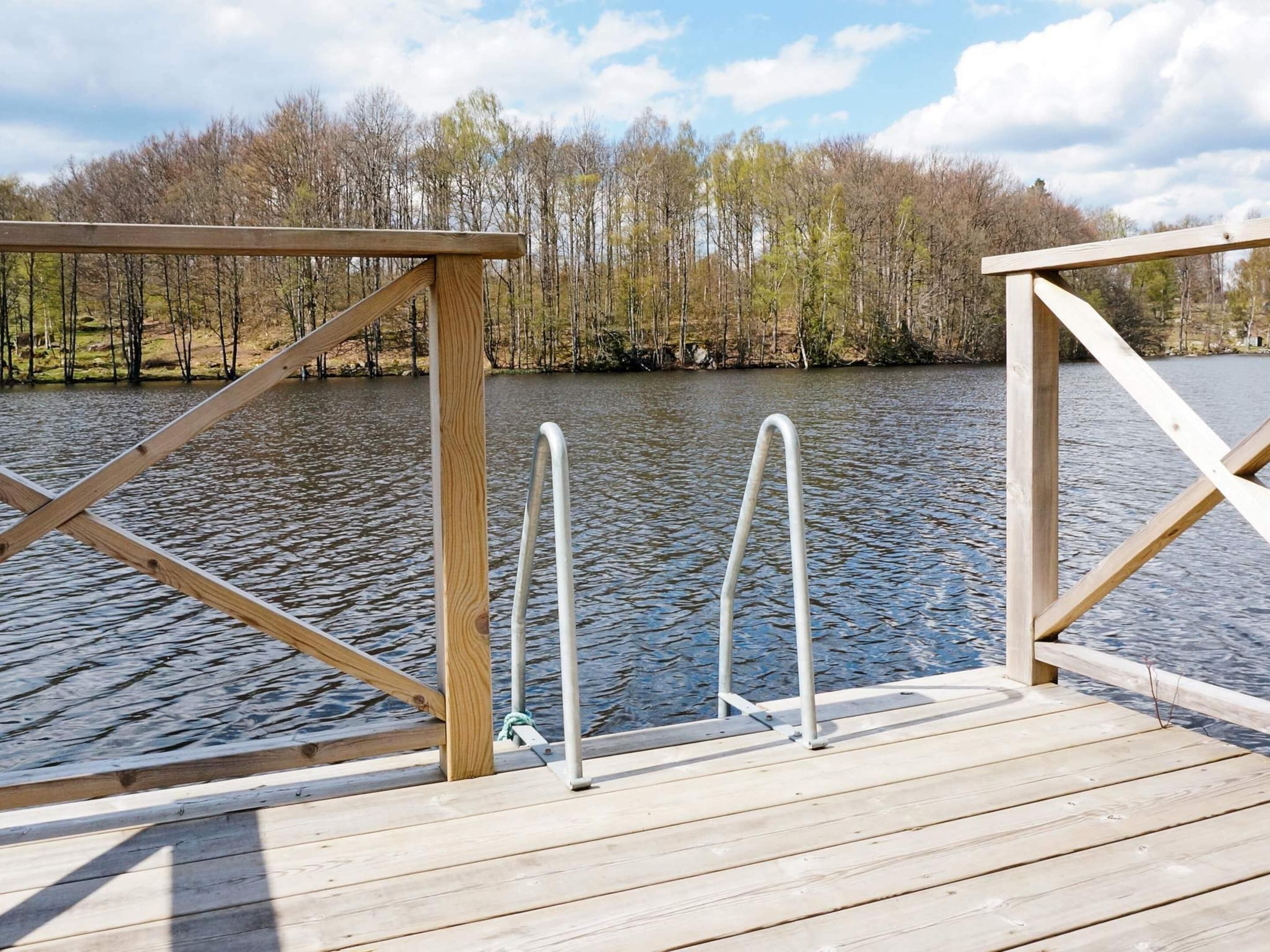 A wooden dock with metal ladders and railings, leading to a calm lake surrounded by trees.