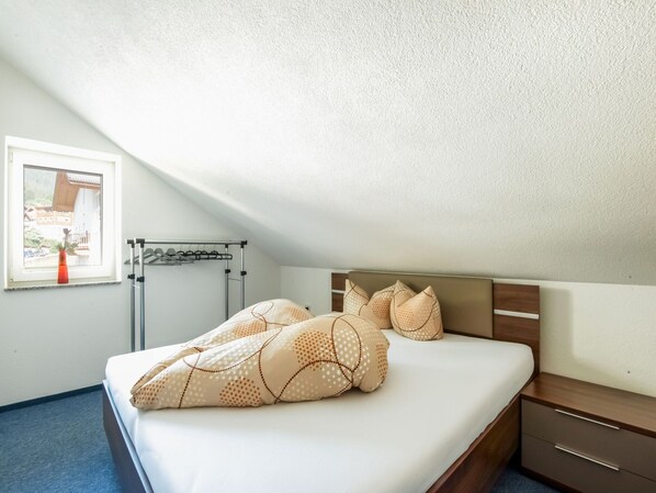 A bedroom with a bed, a wooden nightstand, a window with a view of buildings, and a clothes drying rack.
