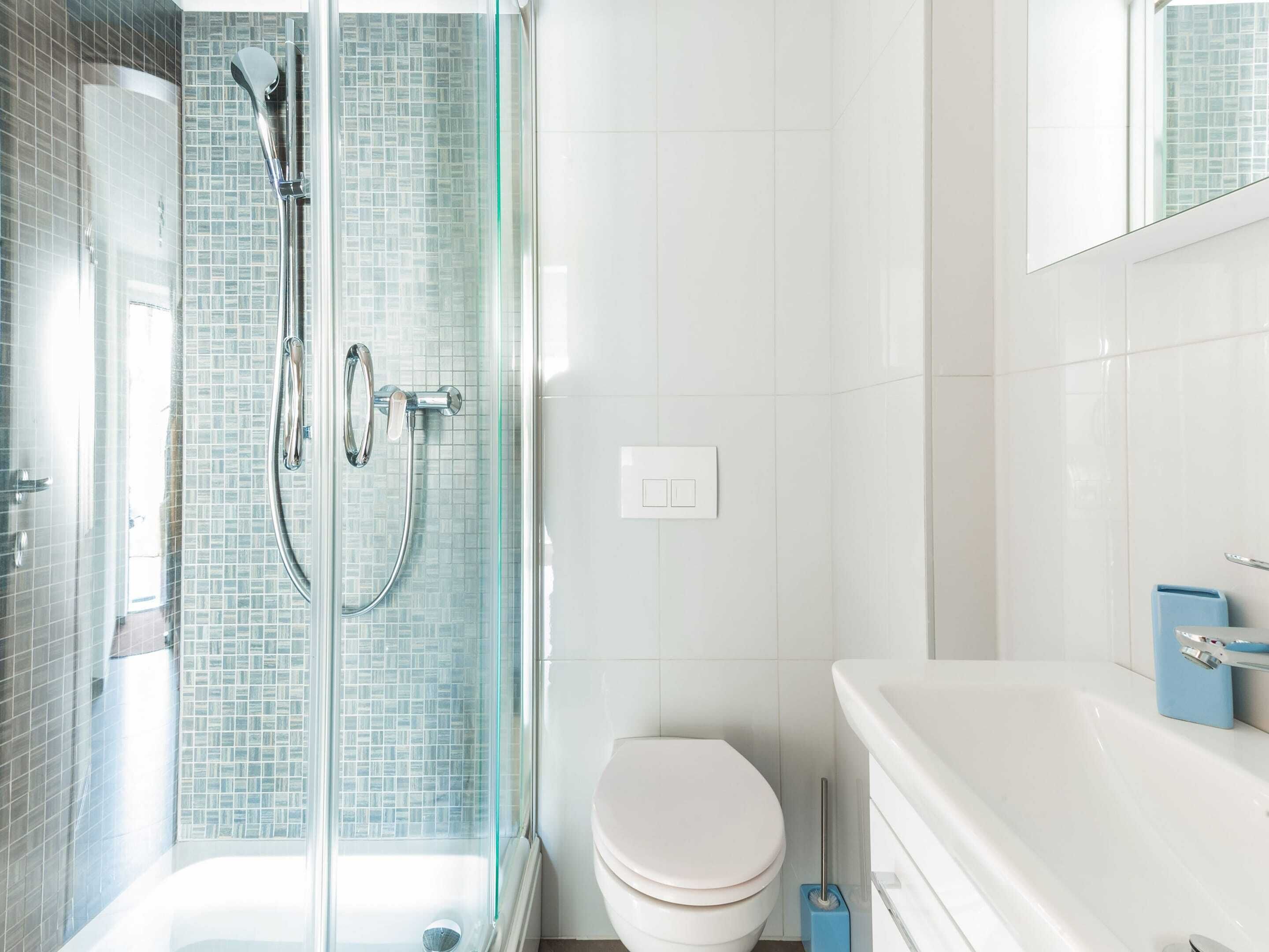 Un baño moderno con ducha de vidrio, inodoro blanco y lavamanos blanco con dispensador de jabón azul.