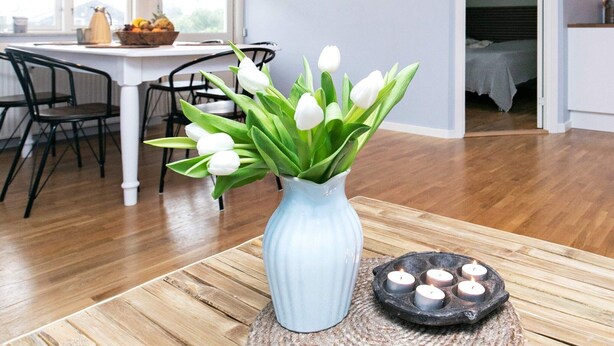 A room with a dining area, a vase with white tulips, and a candle holder on a table. - 2 Person Holiday Home in Blavand (Blavand)