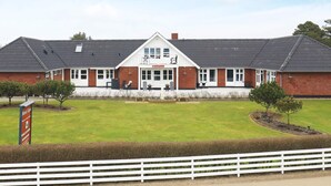 A two-story building with a white facade and a dark roof, labeled 'Motel Garni'. There are outdoor seating areas with tables and chairs, and a well-maintained lawn in front. - 2 Person Holiday Home in Blavand (Blavand)