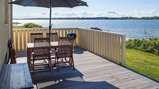 A wooden deck with a table and chairs, a grill, and an umbrella. - 5 Person Holiday Home in Farso (Farso)