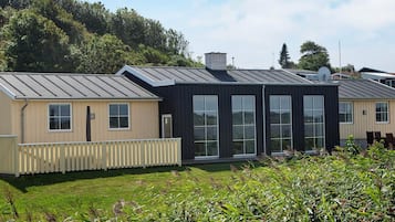 A modern building with large windows and a metal roof, surrounded by greenery.