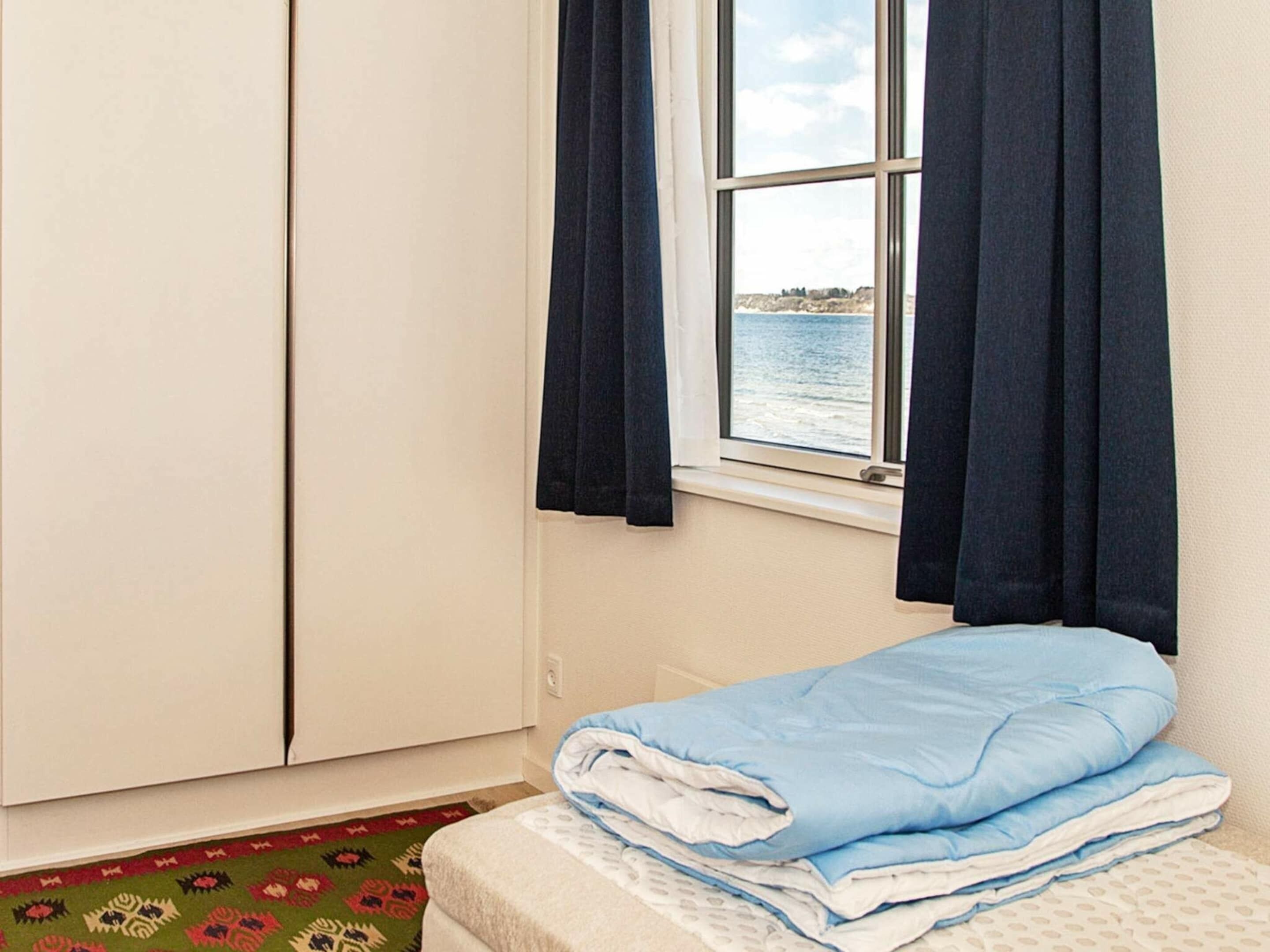 Een slaapkamer met een bed, een raam met gordijnen en uitzicht op zee.
