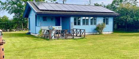 A blue house with a solar panel roof, a fenced patio, and a grassy yard.