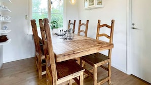 Uma mesa de jantar com seis cadeiras de madeira, um vaso de planta e um castiçal de metal sobre a mesa.