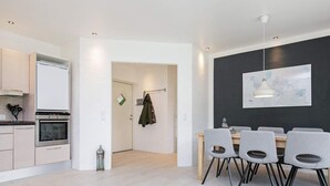 A modern kitchen with built-in appliances, a dining area with grey chairs, and a dark accent wall with a map. - 8 Person Holiday Home in Harboore (Harboore)
