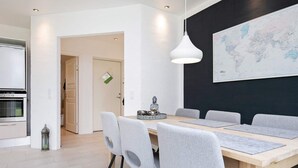 A modern dining area with a wooden table, grey upholstered chairs, and a hanging pendant light. - 8 Person Holiday Home in Harboore (Harboore)