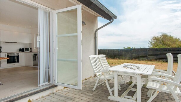 A modern kitchen with white cabinets and appliances, a dining area with white furniture, and a view of the outdoors. - 8 Person Holiday Home in Harboore (Harboore)