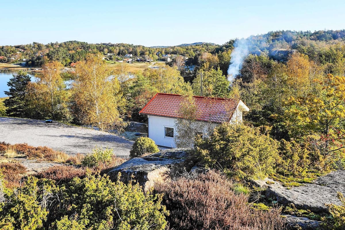 En liten vit byggnad med ett rött tak, omgiven av höstlövsverk och en sjö i bakgrunden.
