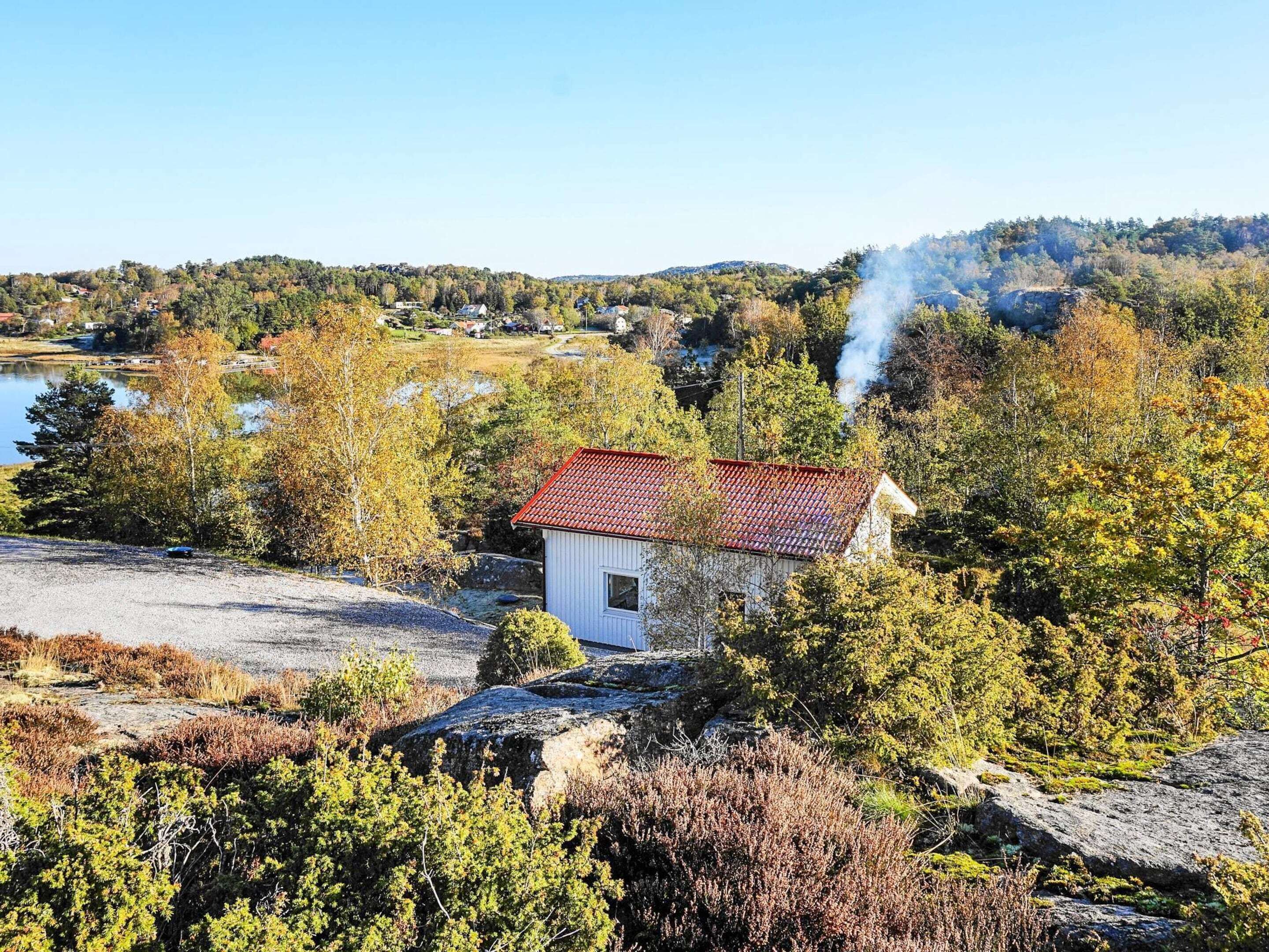 A small white building with a red roof, surrounded by autumn foliage and a lake in the background.