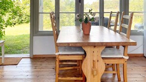 Una mesa de madera con seis sillas, una planta en maceta y una lámpara colgante en una habitación con ventanas amplias.