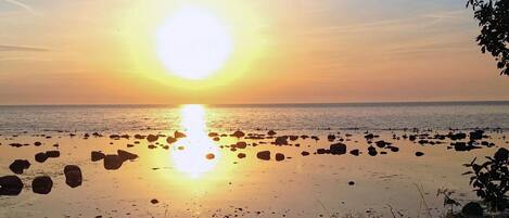 A sunset over a rocky beach with calm water reflecting the sun.