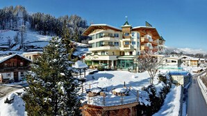 Et hotel med flere etager og balkoner, med en skitraper i baggrunden og et sneklædt landskab.
