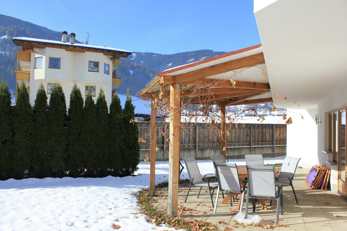 Une terrasse couverte avec des chaises, une clôture en bois et un bâtiment avec une chaîne de montagnes en arrière-plan.