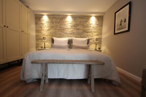 A bedroom with a stone wall headboard, a wooden bench, and a bed with white bedding. - Apartment Haus am Berg, Lonau (Herzberg am Harz)