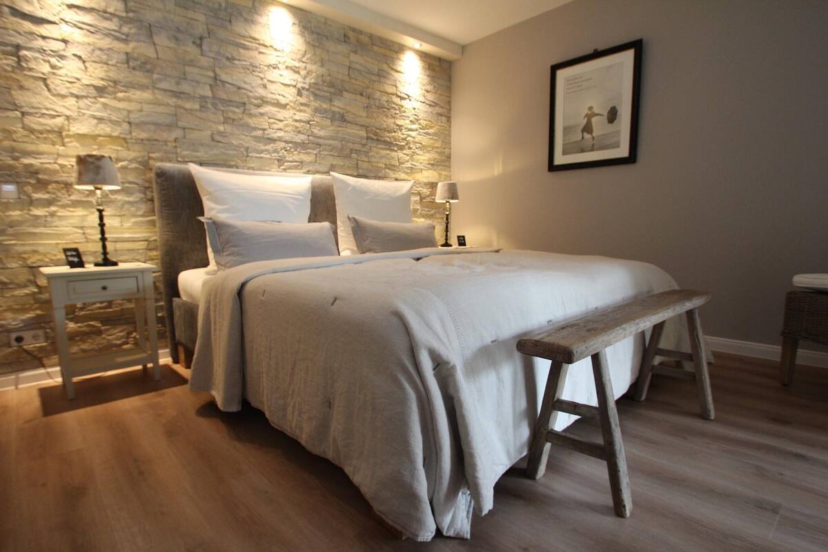 A bedroom with a stone wall, a wooden bench, and a bed with white bedding.