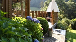 A patio with a brick barbecue area, a wooden fence, and a view of a forested area. - Apartment Haus am Berg, Lonau (Herzberg am Harz)