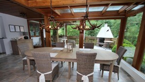 A dining area with a large table and wicker chairs, a wooden ceiling, and a view of the outdoors. - Apartment Haus am Berg, Lonau (Herzberg am Harz)