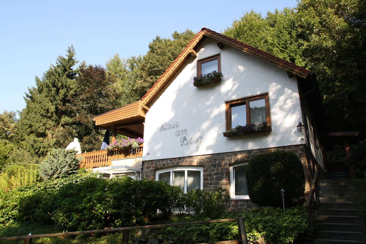 A two-story house with a stone facade, wooden balcony, and a sign that reads "Kaus am Berg."
