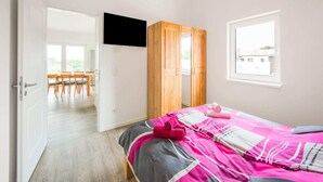 Een slaapkamer met een bed, een aan de muur bevestigde televisie, een raam en een houten garderobe.