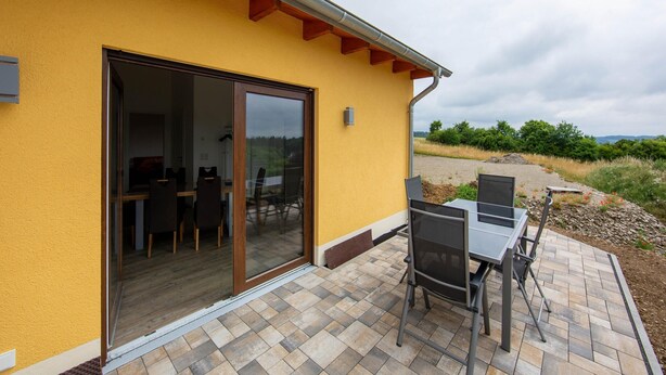A yellow building with a sliding glass door leading to an indoor area with a table and chairs.