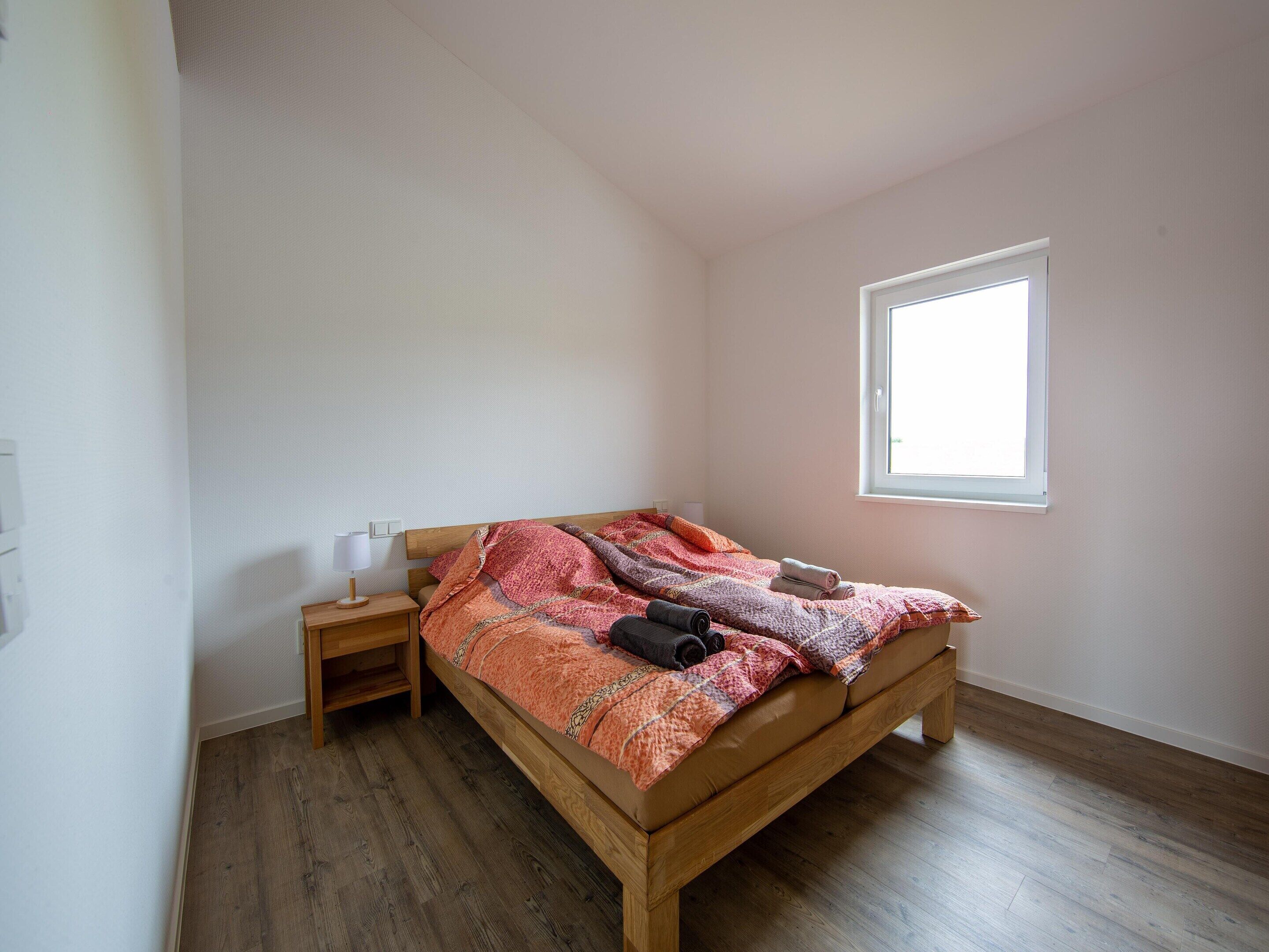 Una cama individual con estructura de madera, una mesita de noche, una ventana y un interruptor de luz en la pared.