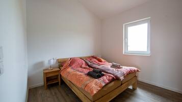 Una cama individual con estructura de madera, una mesita de noche, una ventana y un interruptor de luz en la pared.