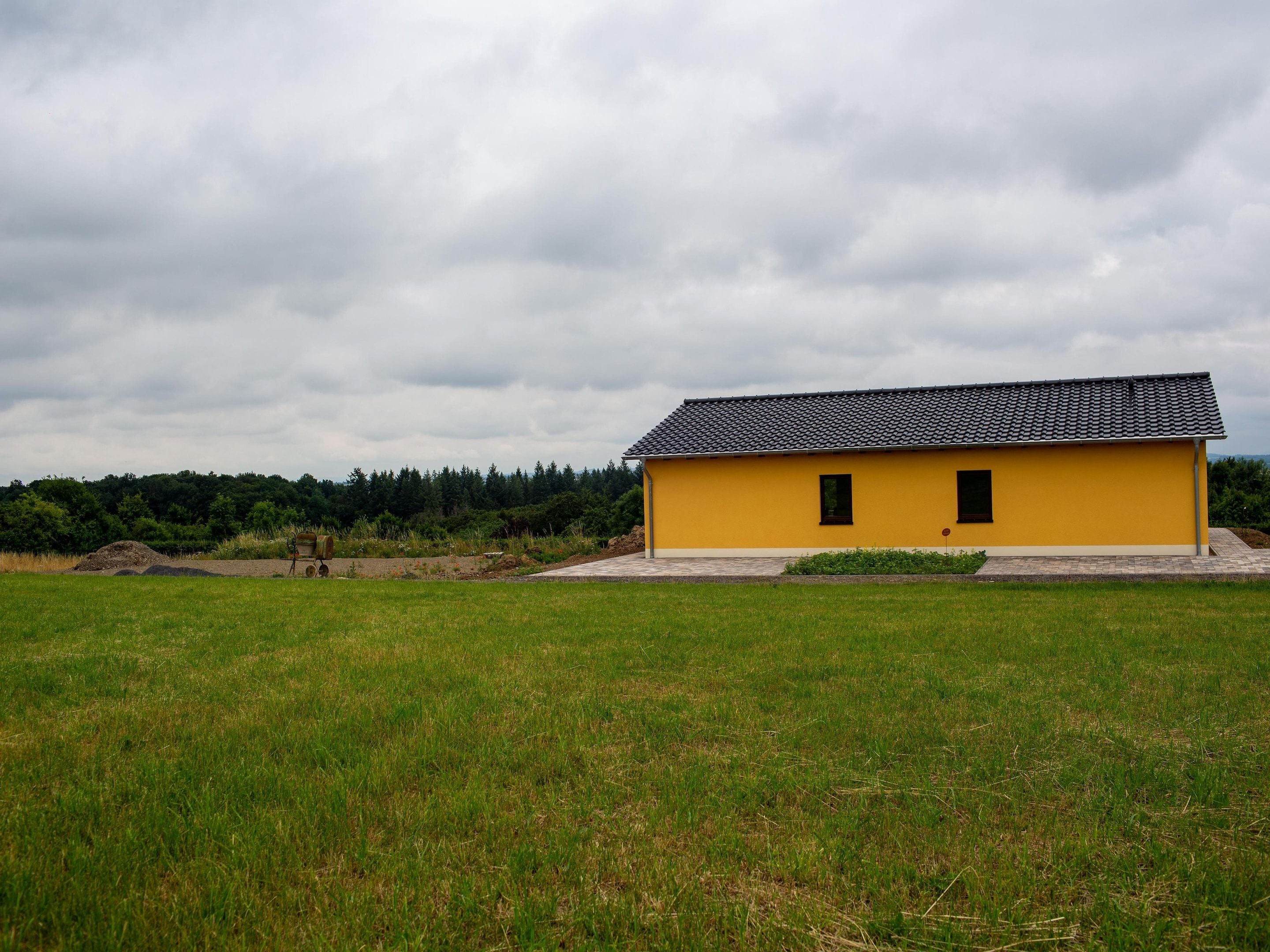 A yellow building with a tiled roof in a grassy field.